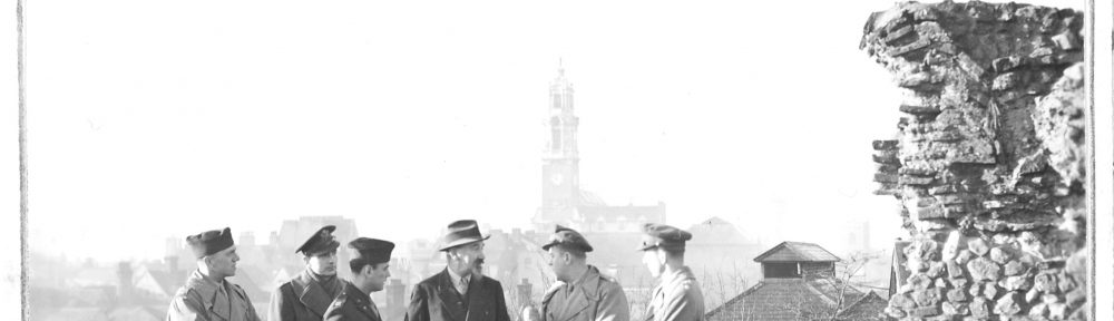 Black and white photogrpah of five men in uniform and another in a smart outfit and trilby hat stood on top of castle walls.